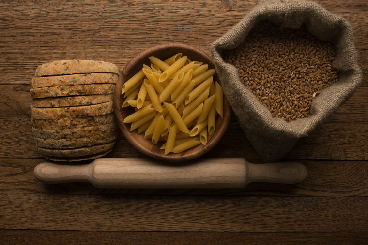 bread, a bowl of pasta and a bag of rice with a roller pin